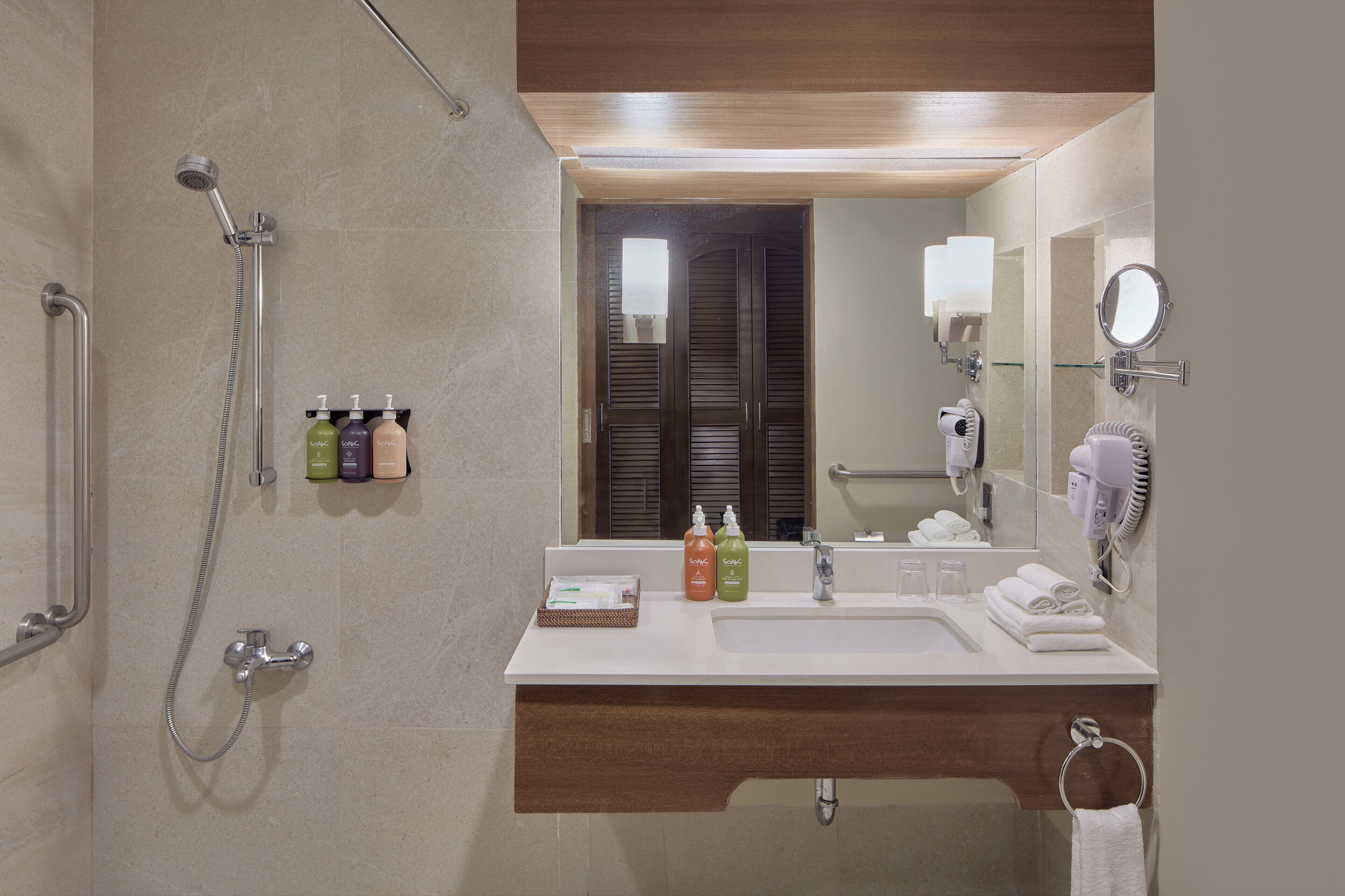 Un baño con ducha, lavabo y espejo. Hay artículos de aseo en el lavabo y un perchero para toallas.