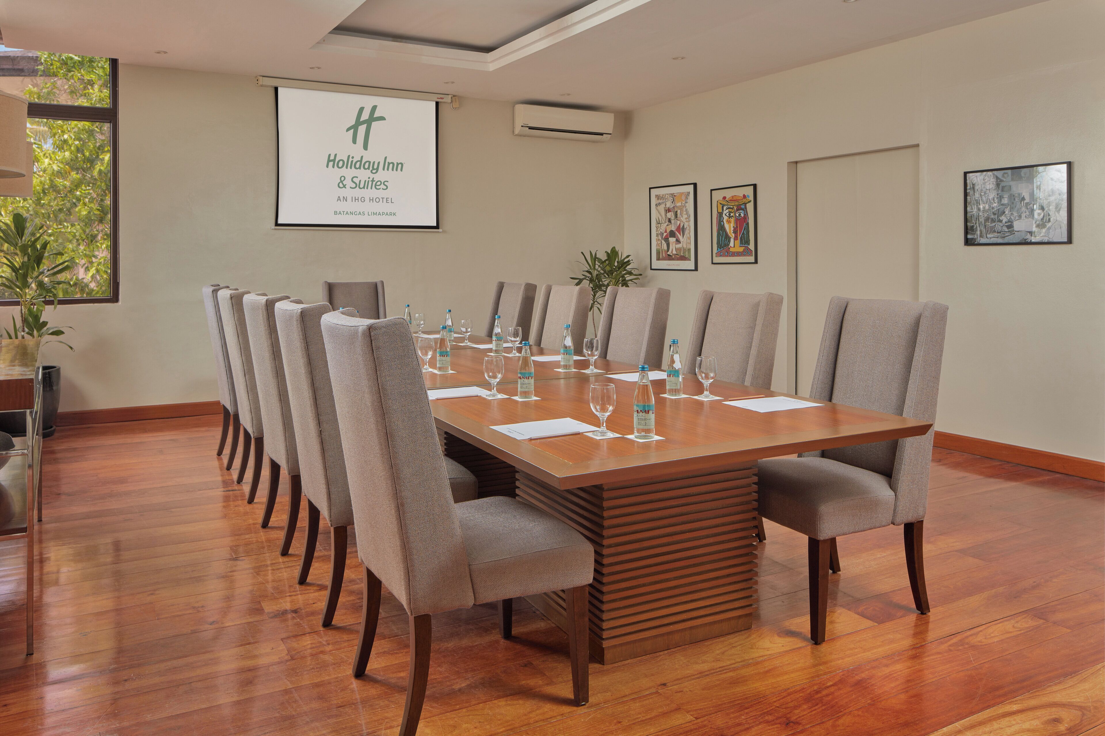 A conference room with a long table, multiple chairs, and a projector screen displaying the hotel name.