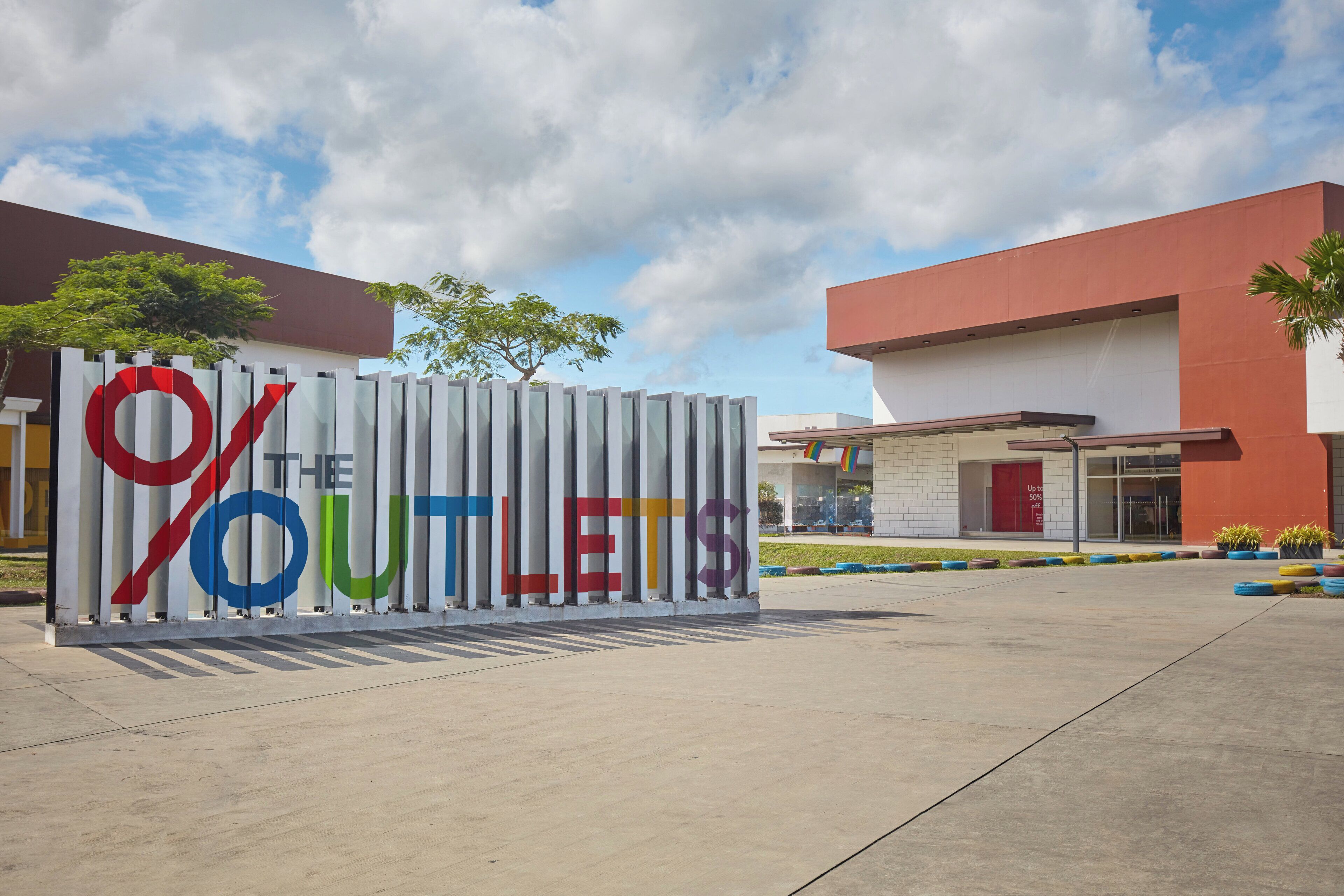 Un cartel con el texto '% THE OUTLETS' frente a un edificio de techo rojo y entrada de vidrio.