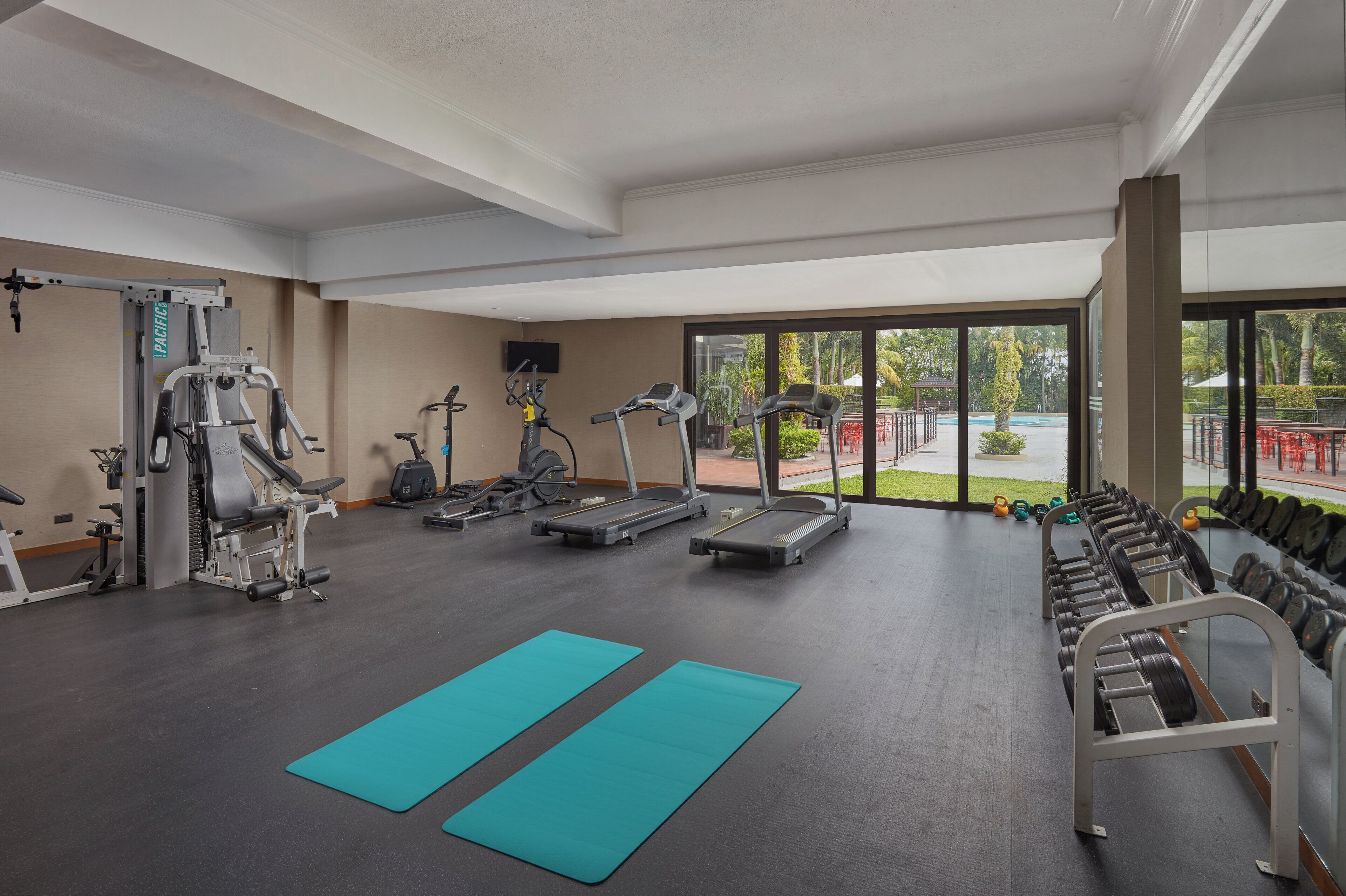 Un gimnasio con equipo de ejercicio, un televisor y vistas al exterior.