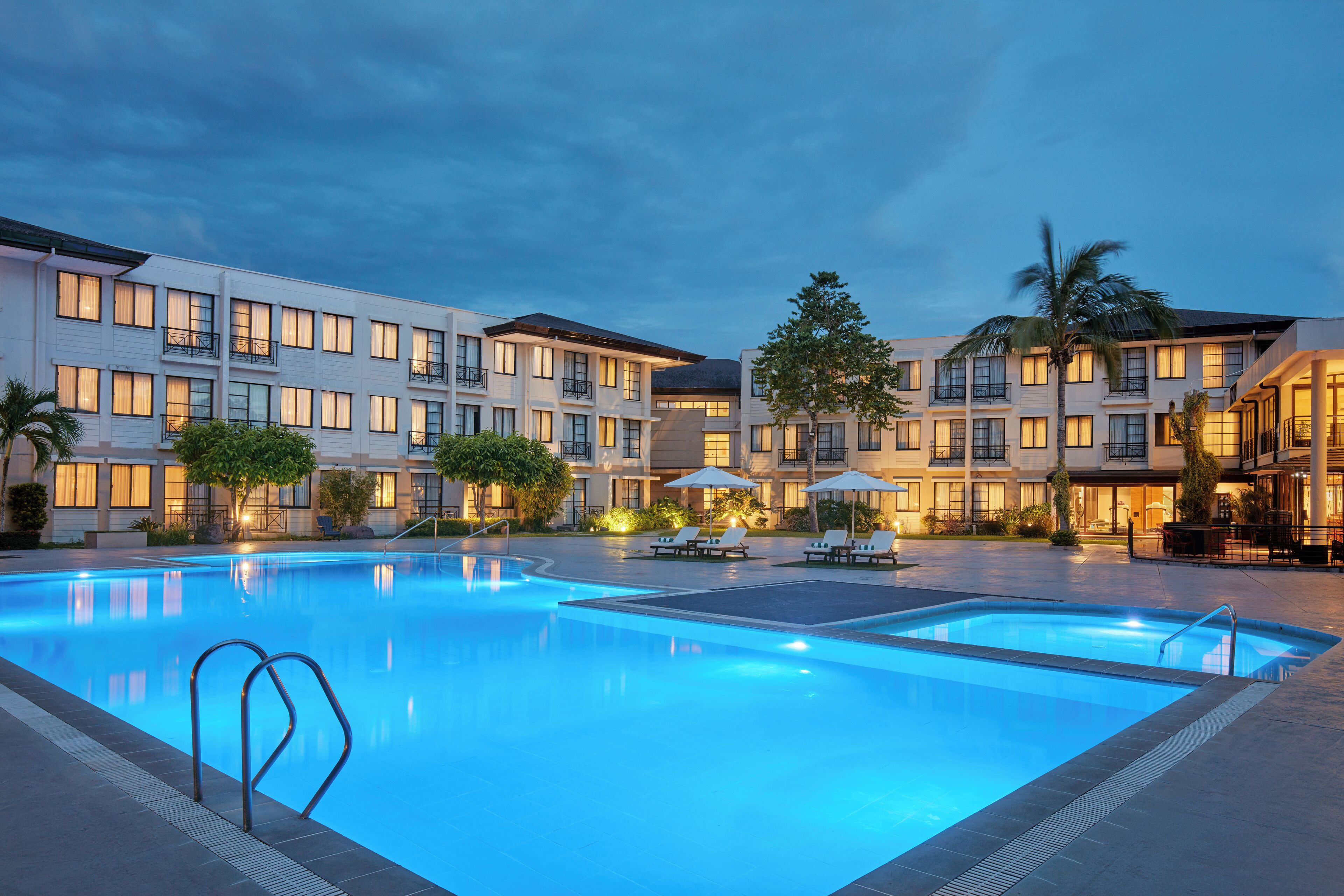 Un hotel con piscina, varios balcones y zonas de estar al aire libre.