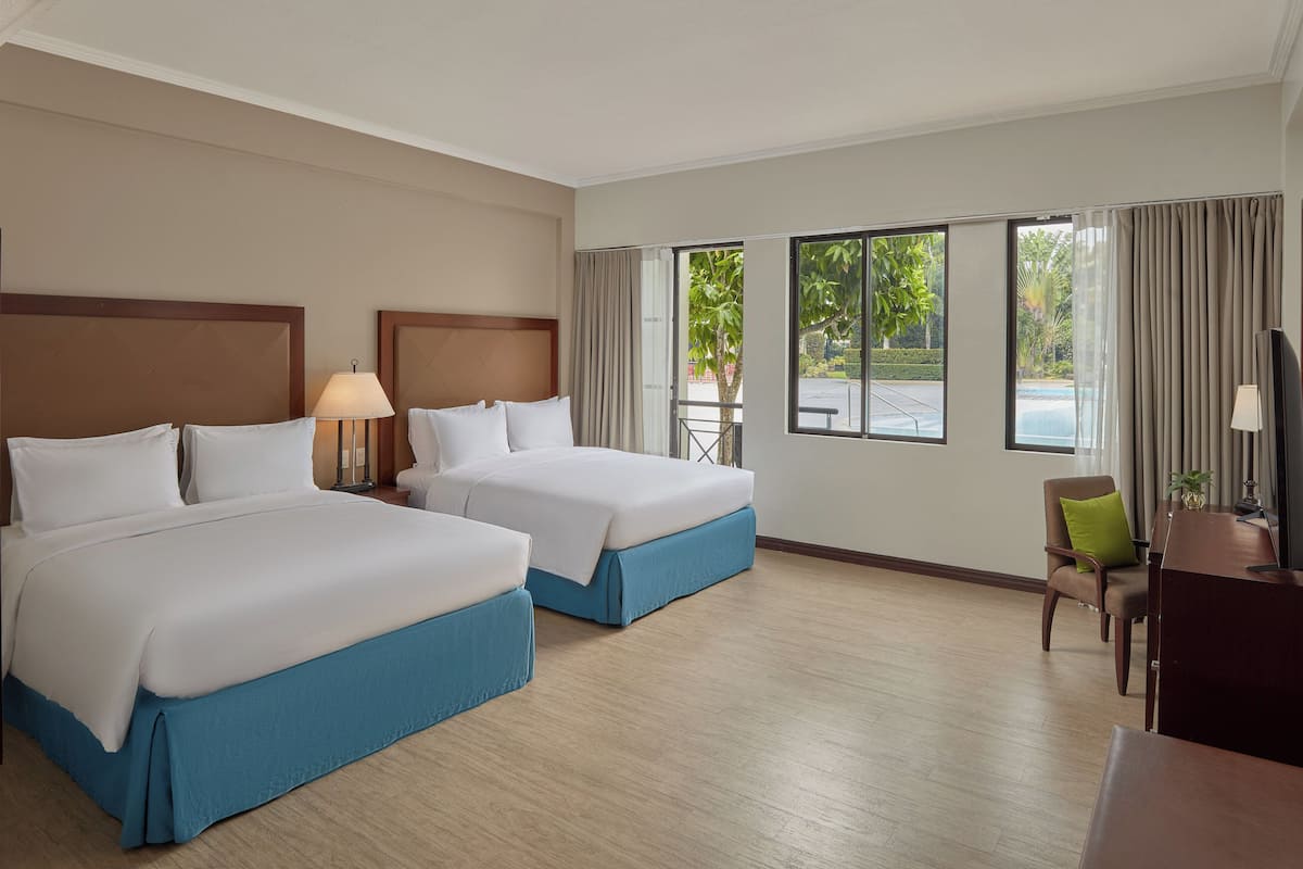 A hotel room with two beds, a desk, a chair, and a TV.