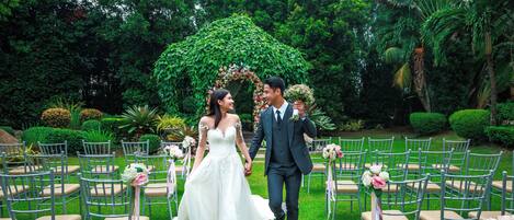 A wedding ceremony outdoors with a floral arch and chairs arranged in rows.