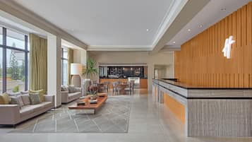 Relax in our spacious lobby, featuring a reception desk, seating area, dining space, and large windows offering views of the outdoors.