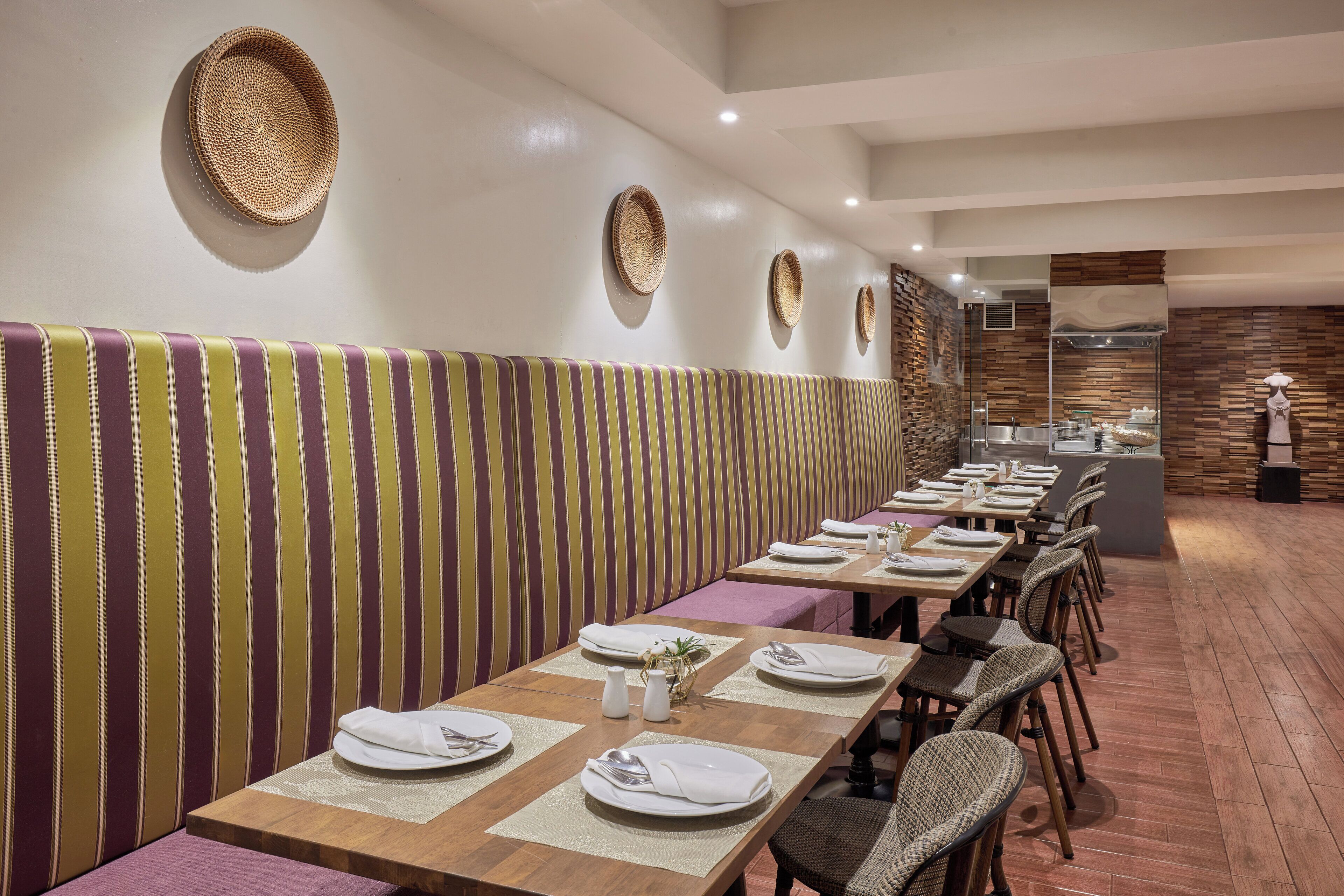 A restaurant with striped booth seating, wooden tables, and woven wall decorations.