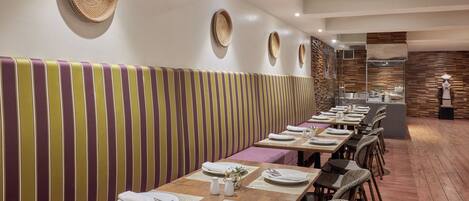 A restaurant with striped booth seating, wooden tables, and woven wall decorations.