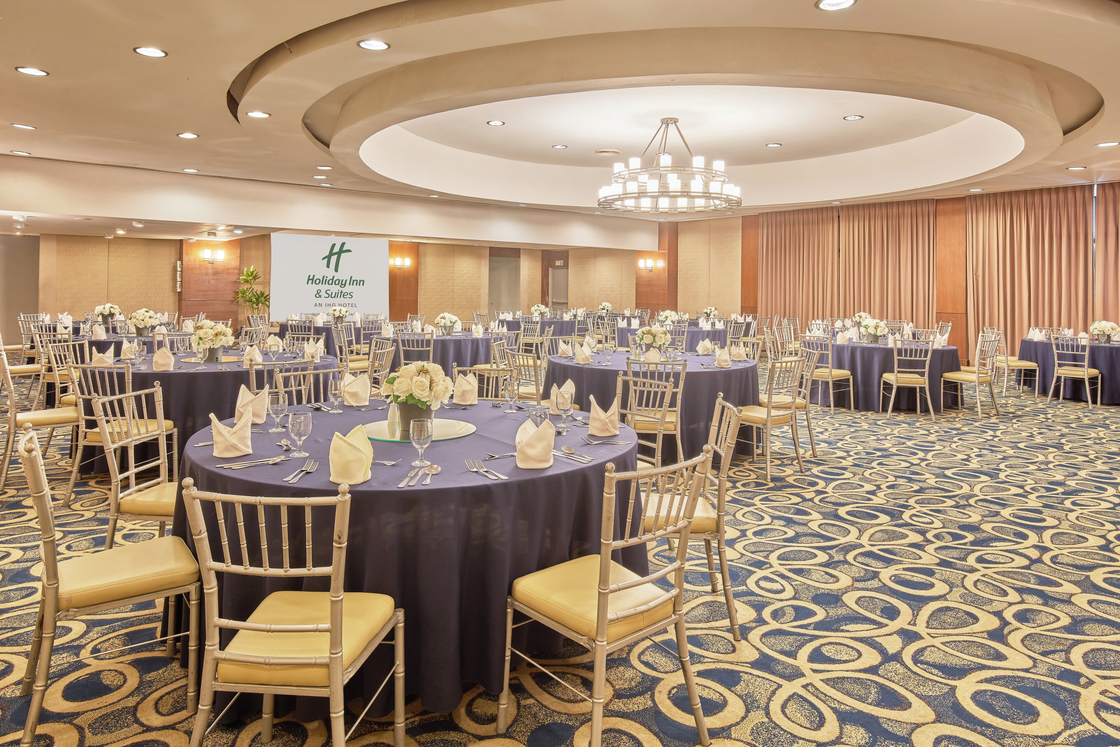 Un salón de banquetes con mesas redondas, sillas y una araña.