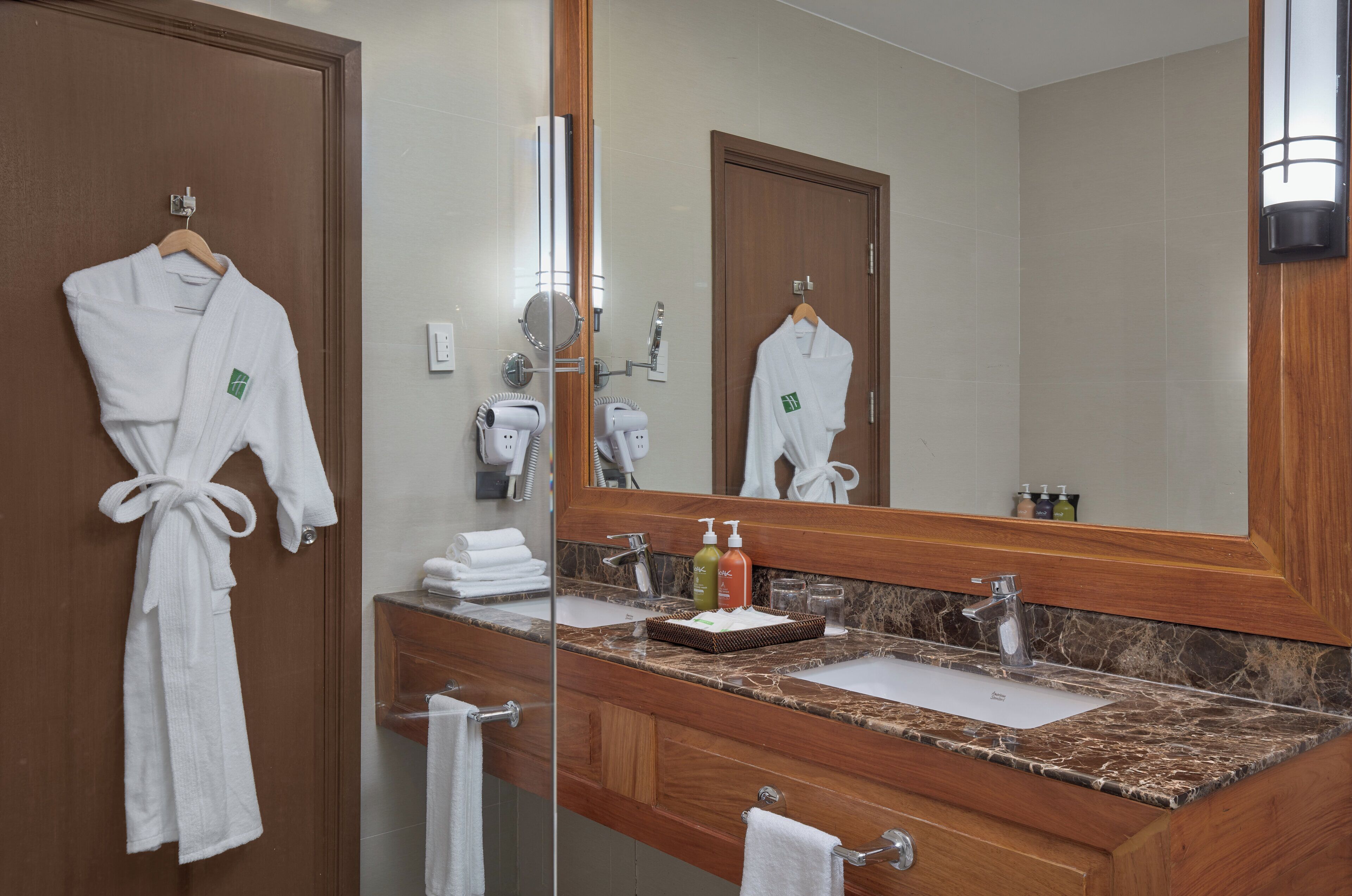 Un baño con tocador de madera, un espejo grande y dos albornoces blancos colgados en la pared.