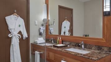 A bathroom with a wooden vanity, a large mirror, and two white robes hanging on the wall.