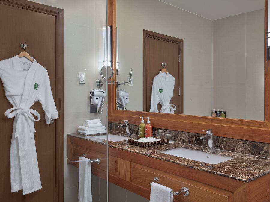 A bathroom with a wooden vanity, a large mirror, and two white robes hanging on the wall.