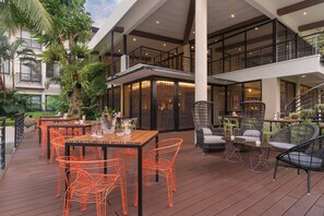 An outdoor dining area with tables and chairs, surrounded by lush greenery and a modern building structure. - Holiday Inn & Suites Batangas Limapark by IHG (Malvar)