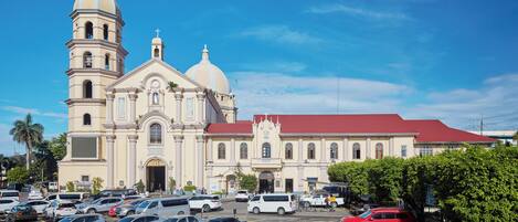 A large church with two domes and a bell tower, surrounded by a parking lot with various cars.