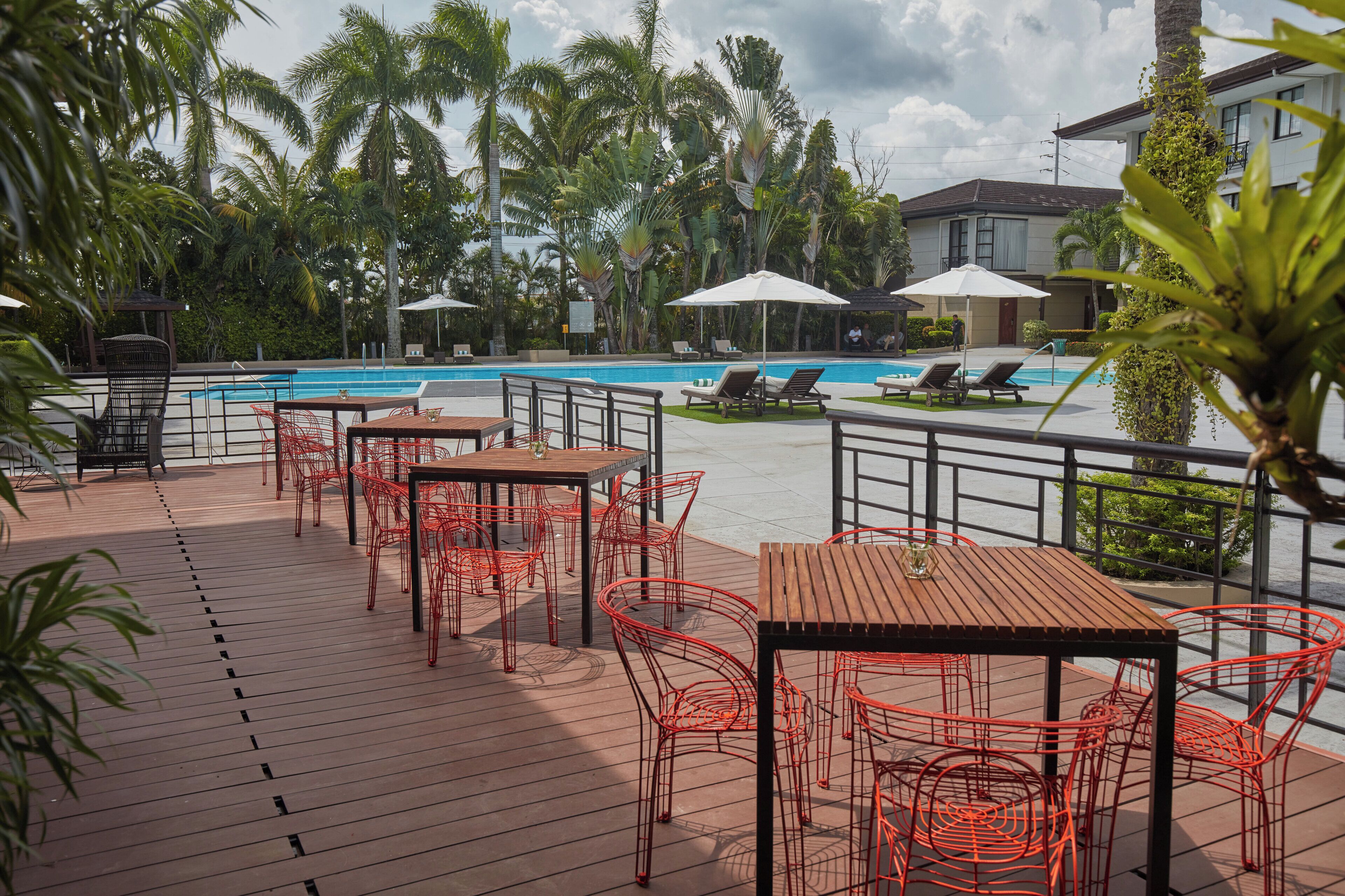 A poolside area with red metal chairs and tables, a swimming pool, and palm trees.