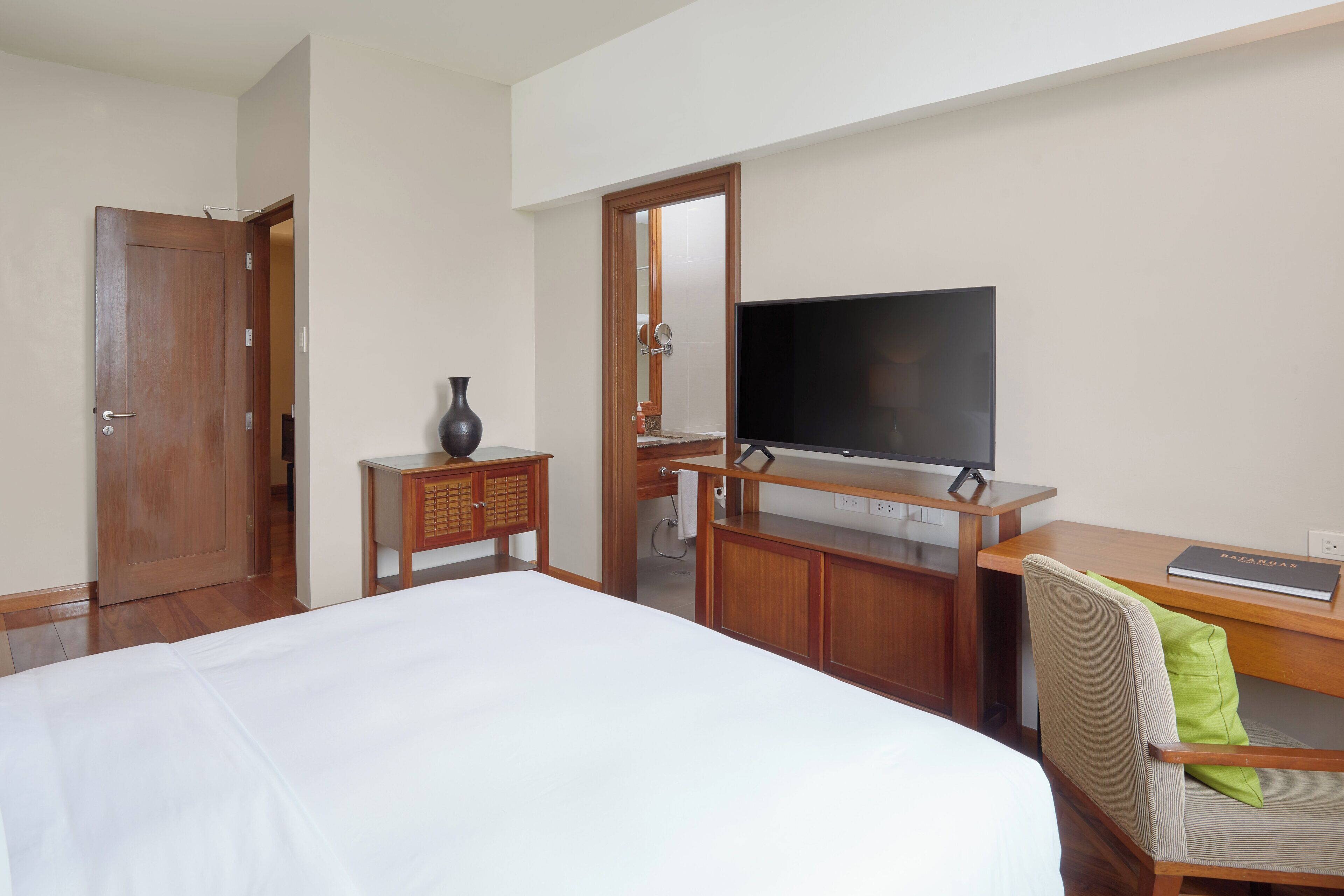 A hotel room with a bed, a desk with a flat-screen TV, a mirror, and a wooden wardrobe.