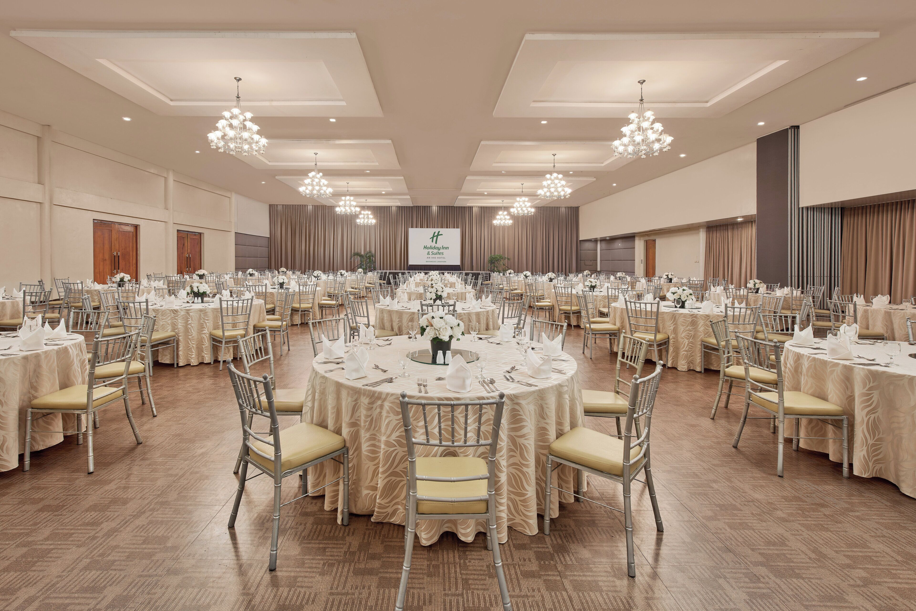 A large banquet hall with round tables, chairs, and chandeliers.