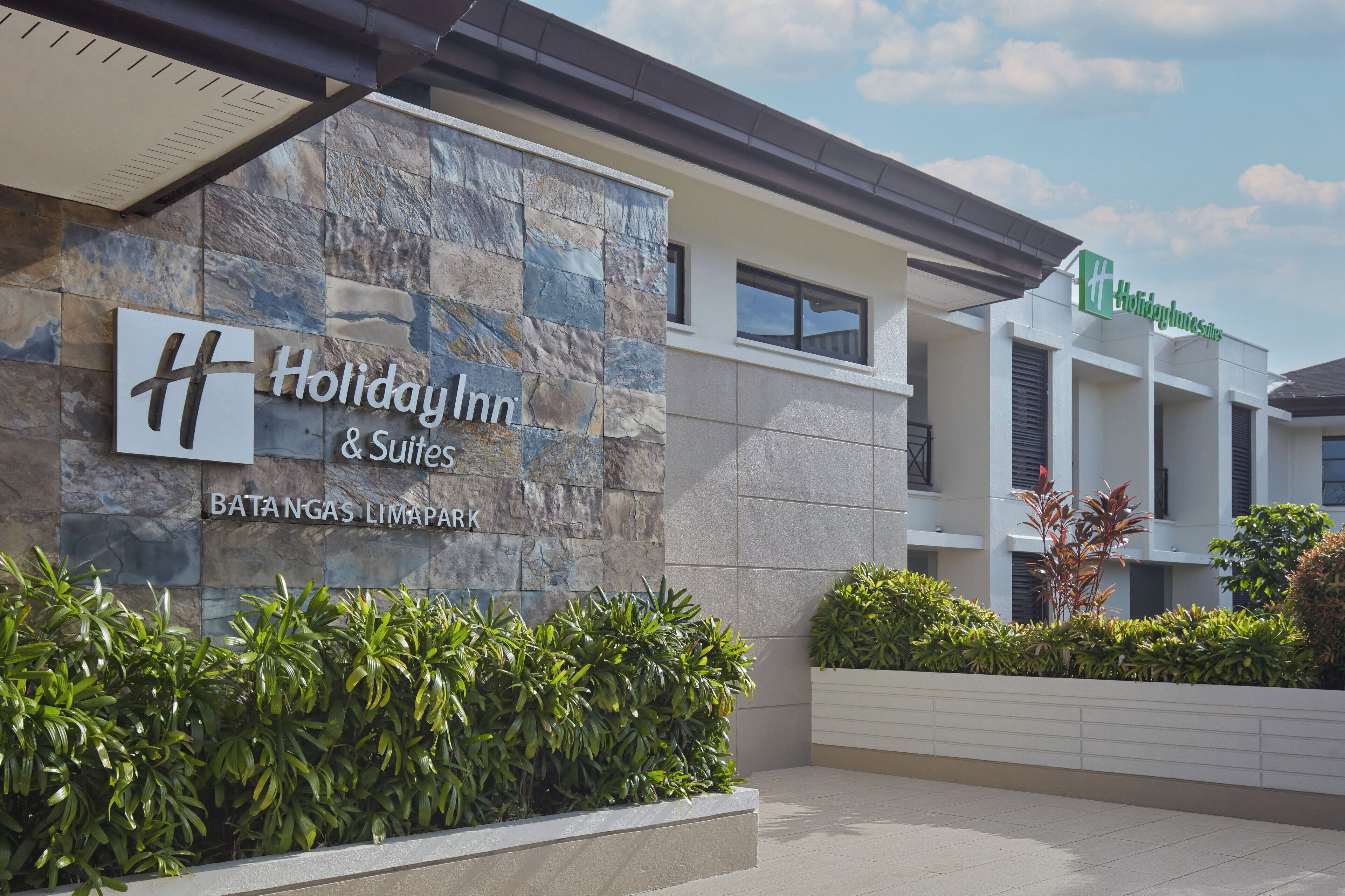 Letrero de Holiday Inn & Suites, con fachada de piedra y un edificio moderno al fondo.