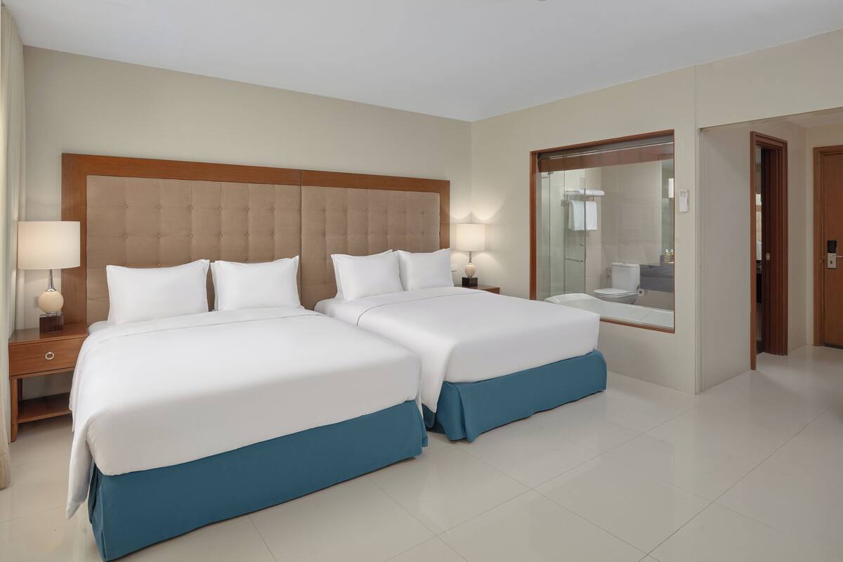 A hotel room with two beds, a large mirror, and a bathroom visible through a glass door.