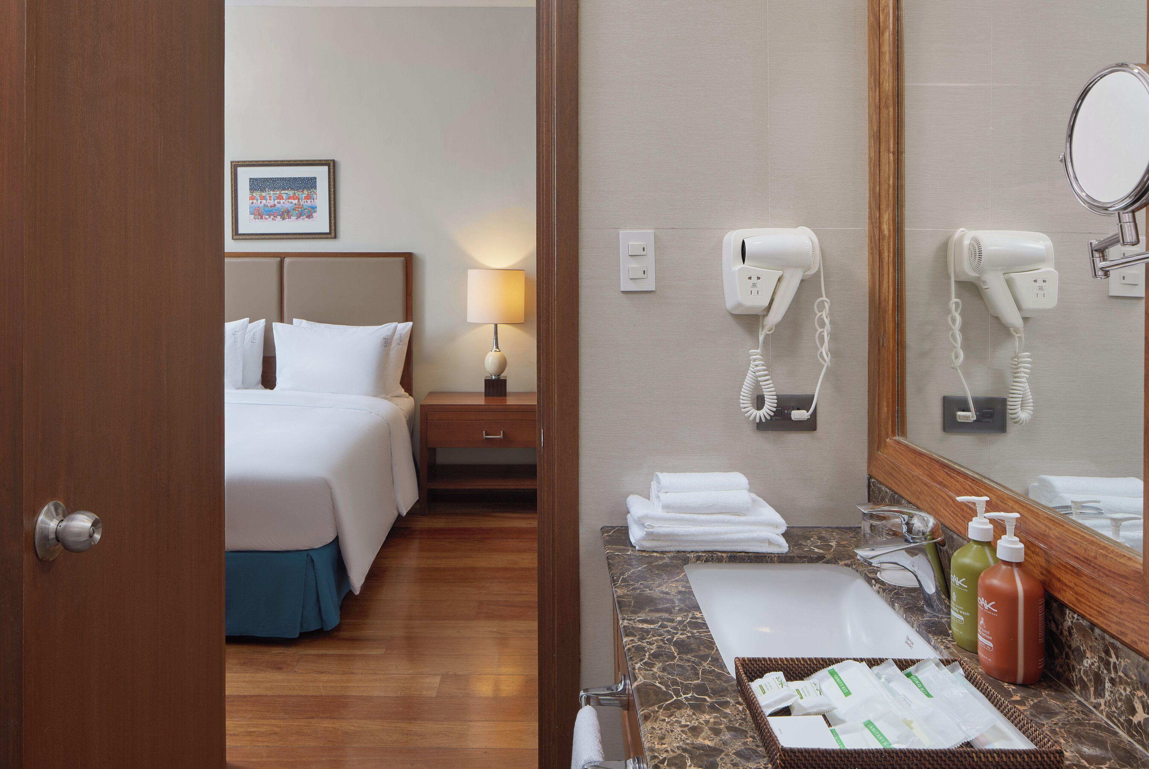 Habitación de hotel con cama, mesita de noche, lámpara, secador de pelo, espejo y artículos de baño.