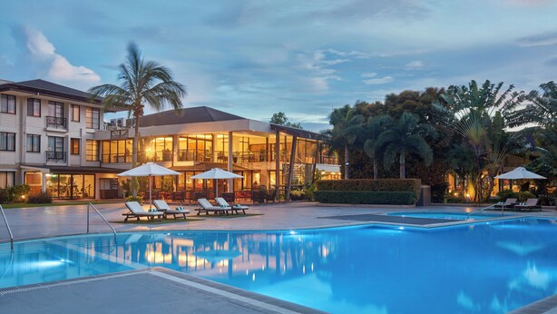A swimming pool with lounge chairs and umbrellas, a building with balconies, and palm trees. - Holiday Inn & Suites Batangas Limapark by IHG (Malvar)