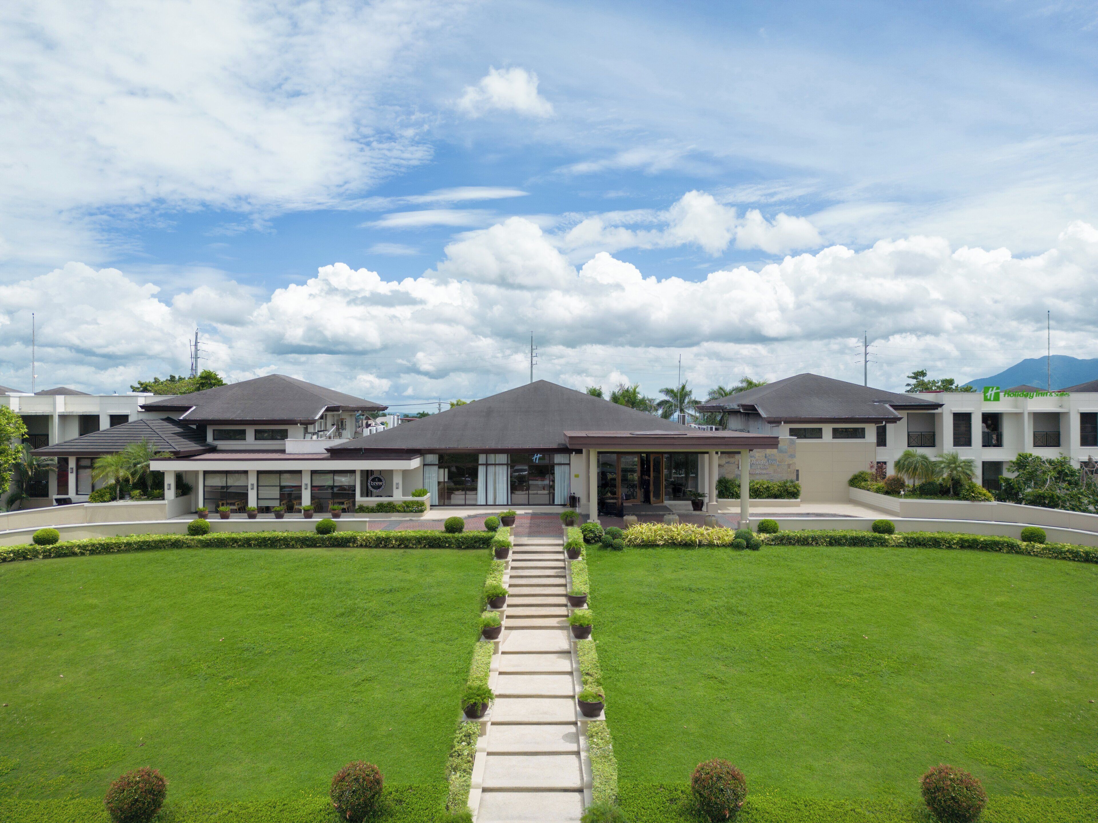 A hotel with a central entrance, a covered walkway, and a well-maintained lawn.
