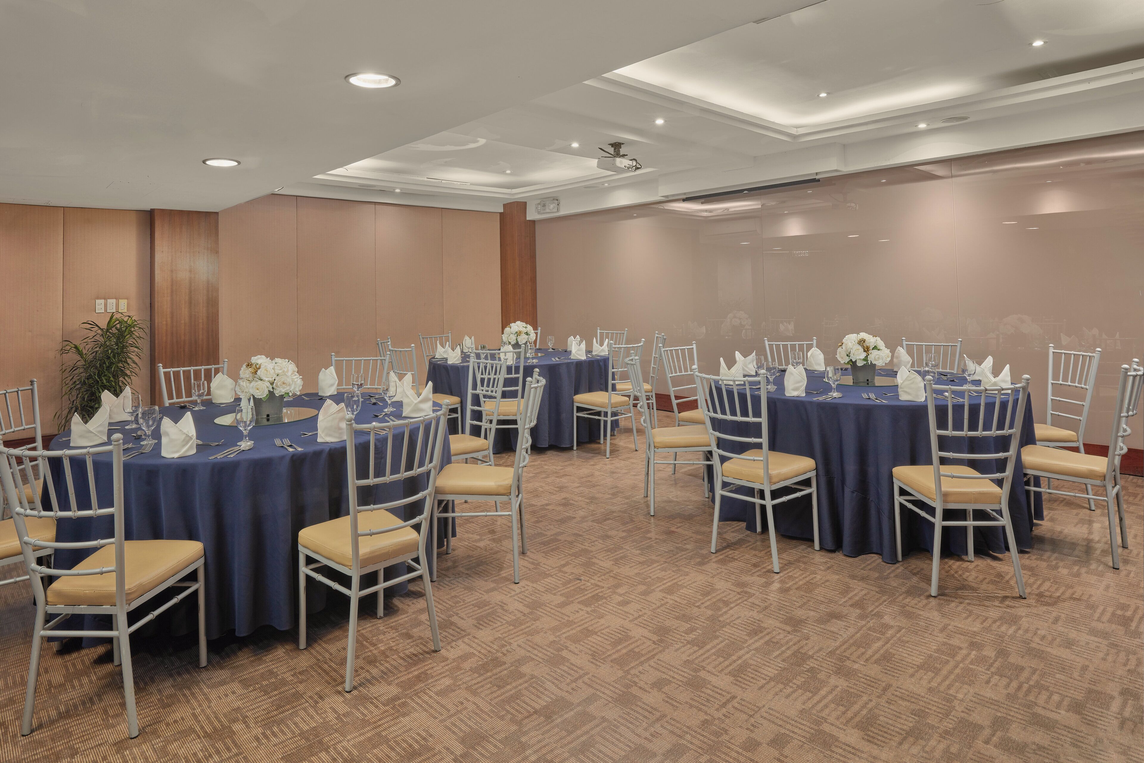 A conference room with round tables, white chairs, and blue tablecloths.
