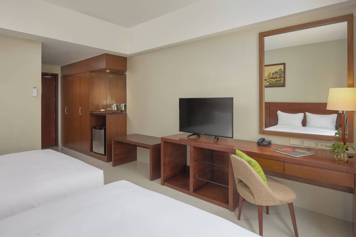 A hotel room with two beds, a desk with a TV, a chair, a desk lamp, and a large mirror.