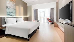 A modern hotel room with a large bed, a flat-screen TV, a desk with a chair, and a balcony with curtains. - Holiday Inn Express Qidong Economic Zone by IHG (Nantong)