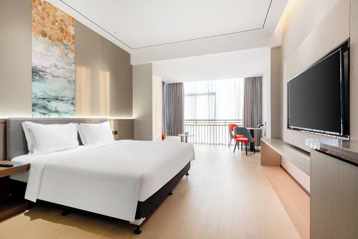 Una habitación de hotel moderna con una cama grande, un televisor de pantalla plana, un escritorio con una silla y un balcón con cortinas.