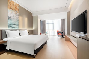 Una habitación de hotel moderna con una cama grande, un televisor de pantalla plana, un escritorio con una silla y un balcón con cortinas.