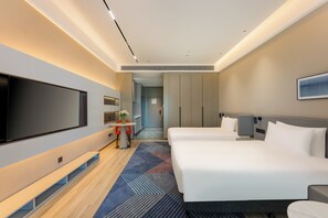 A hotel room with a large flat-screen TV, two beds, a small table with a vase, and a hallway leading to a bathroom. - Holiday Inn Express Qidong Economic Zone by IHG (Nantong)
