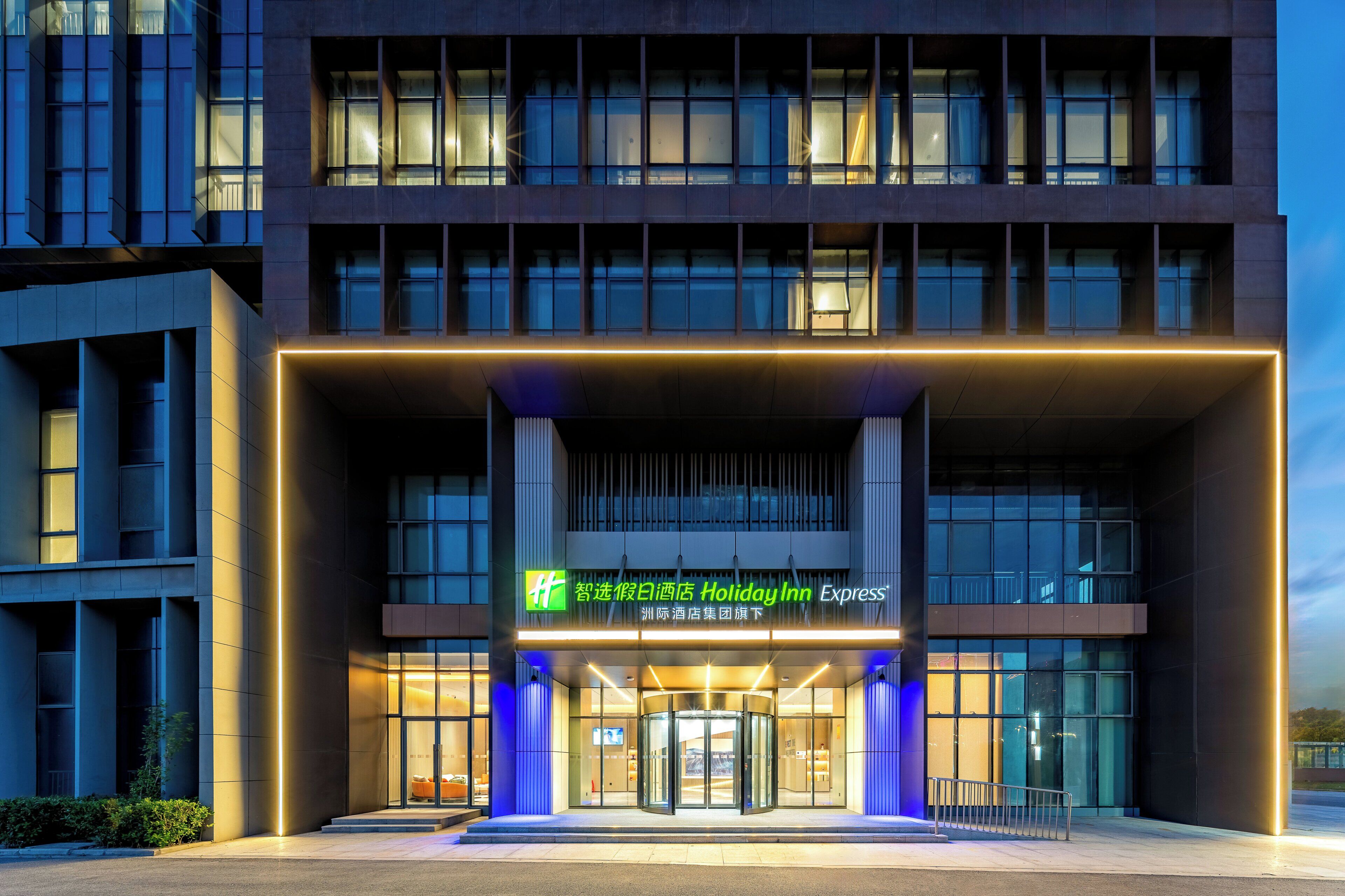 A modern hotel entrance with a revolving door, illuminated signage, and a glass facade.