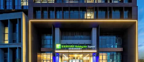 A modern hotel entrance with a revolving door, illuminated signage, and a glass facade.