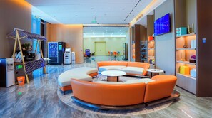 A modern lobby with a curved orange sofa, a round coffee table, vending machines, and a TV on the wall. - Holiday Inn Express Qidong Economic Zone by IHG (Nantong)