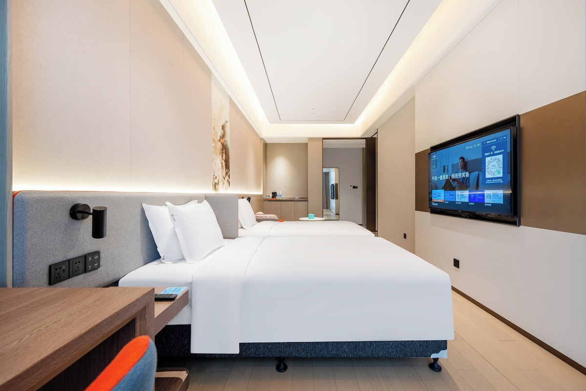Una habitación de hotel moderna con una cama grande, un escritorio, un televisor de pantalla plana montado en la pared y una lámpara de techo.
