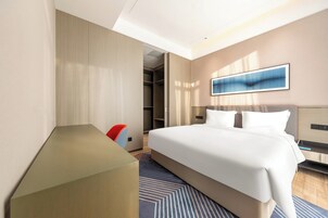 A modern hotel room with a large bed, a desk, and a walk-in closet.