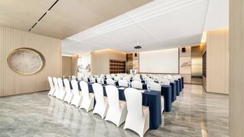 A conference room with rows of tables and chairs, a projector screen, and a large circular wall decoration.