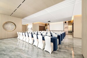 A conference room with rows of tables and chairs, a projector screen, and a large circular wall decoration. - Holiday Inn Express Qidong Economic Zone by IHG (Nantong)