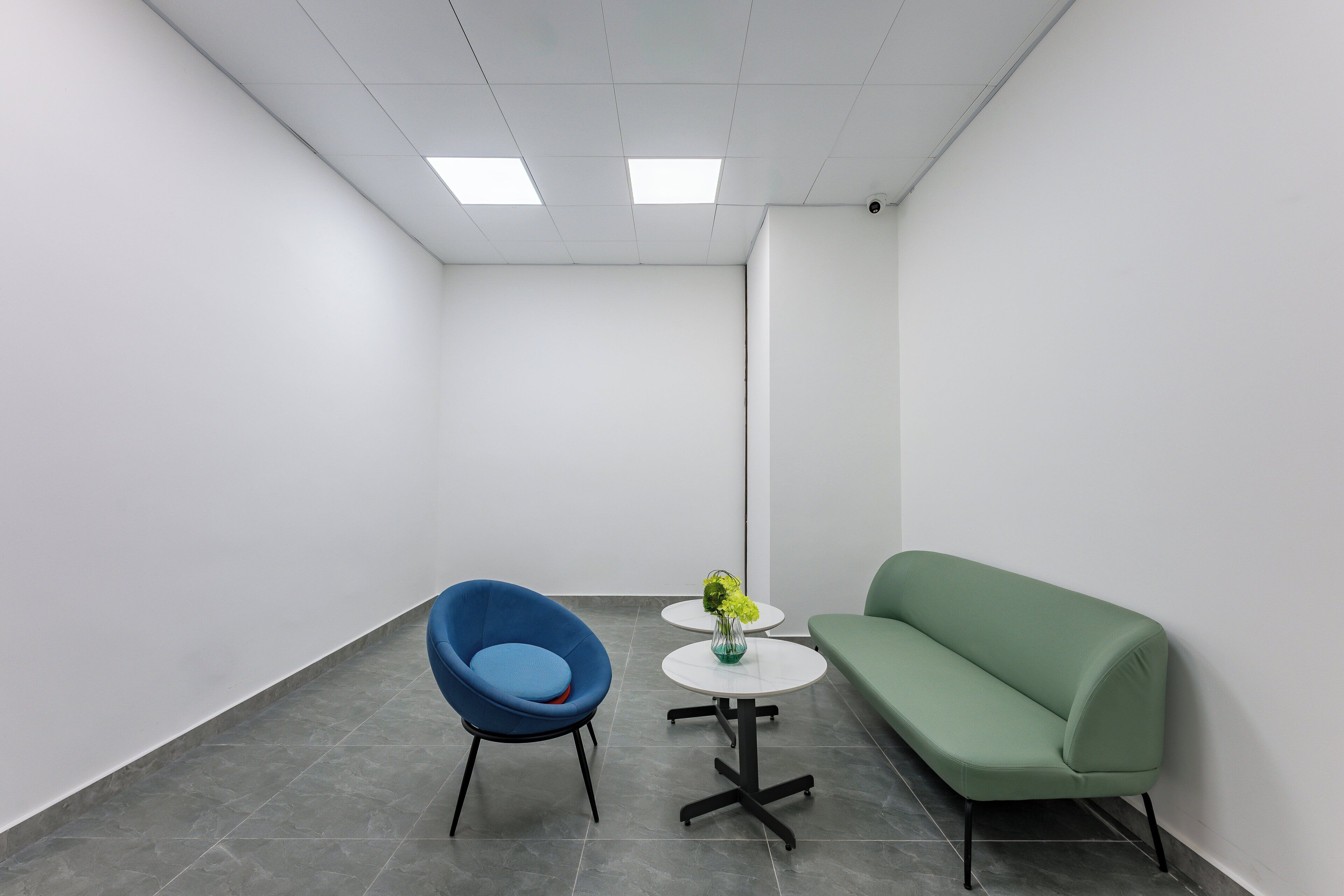 A modern office space with a blue chair, a green sofa, and a small white table with a vase.