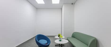 A modern office space with a blue chair, a green sofa, and a small white table with a vase.