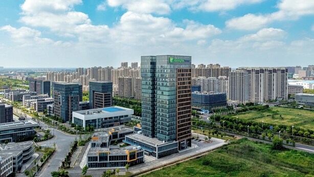 A modern high-rise building with a glass facade, surrounded by other high-rise buildings and a green park area. - Holiday Inn Express Qidong Economic Zone by IHG (Nantong)