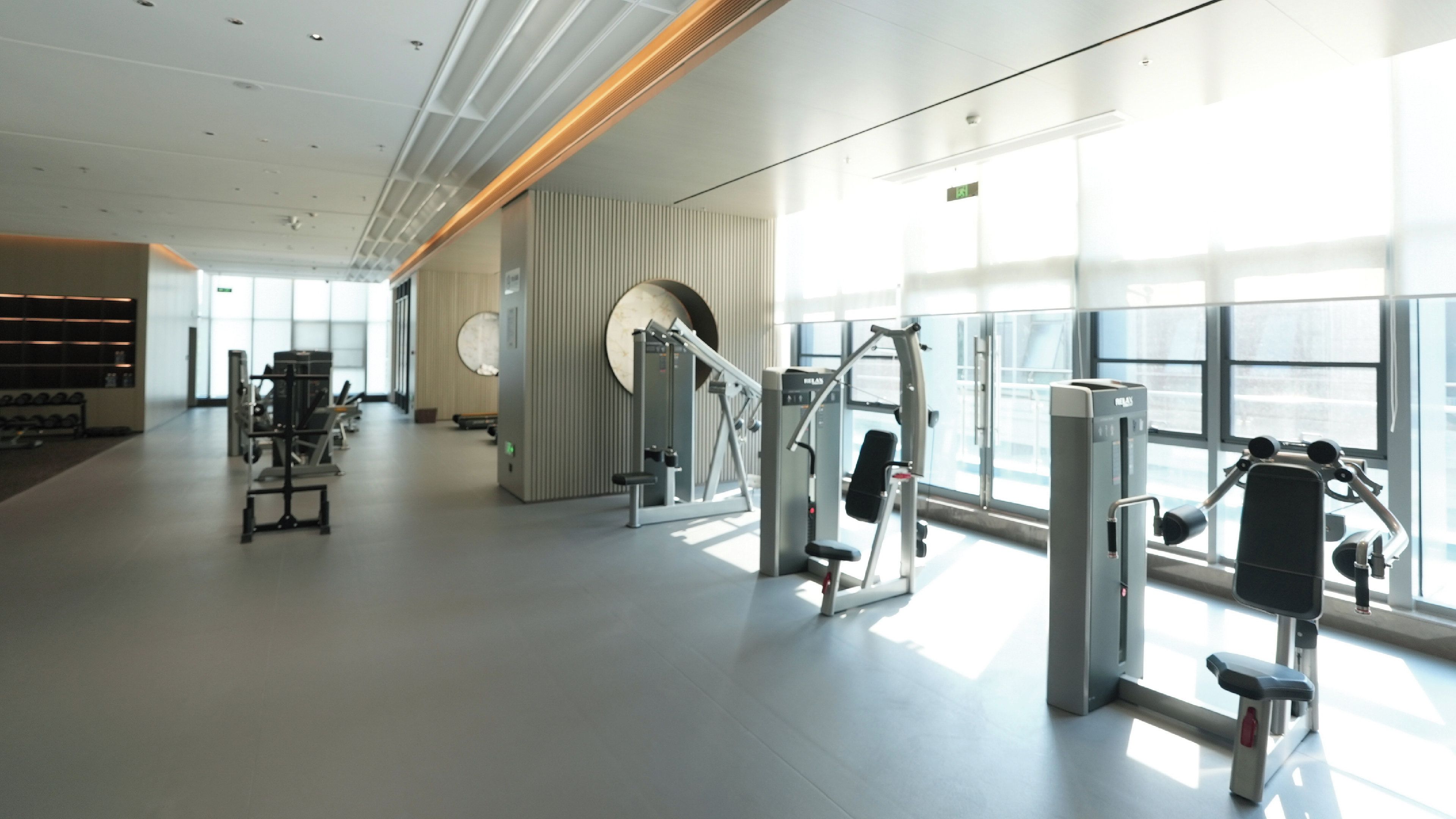A spacious gym with various exercise machines, large windows, and a modern interior design.