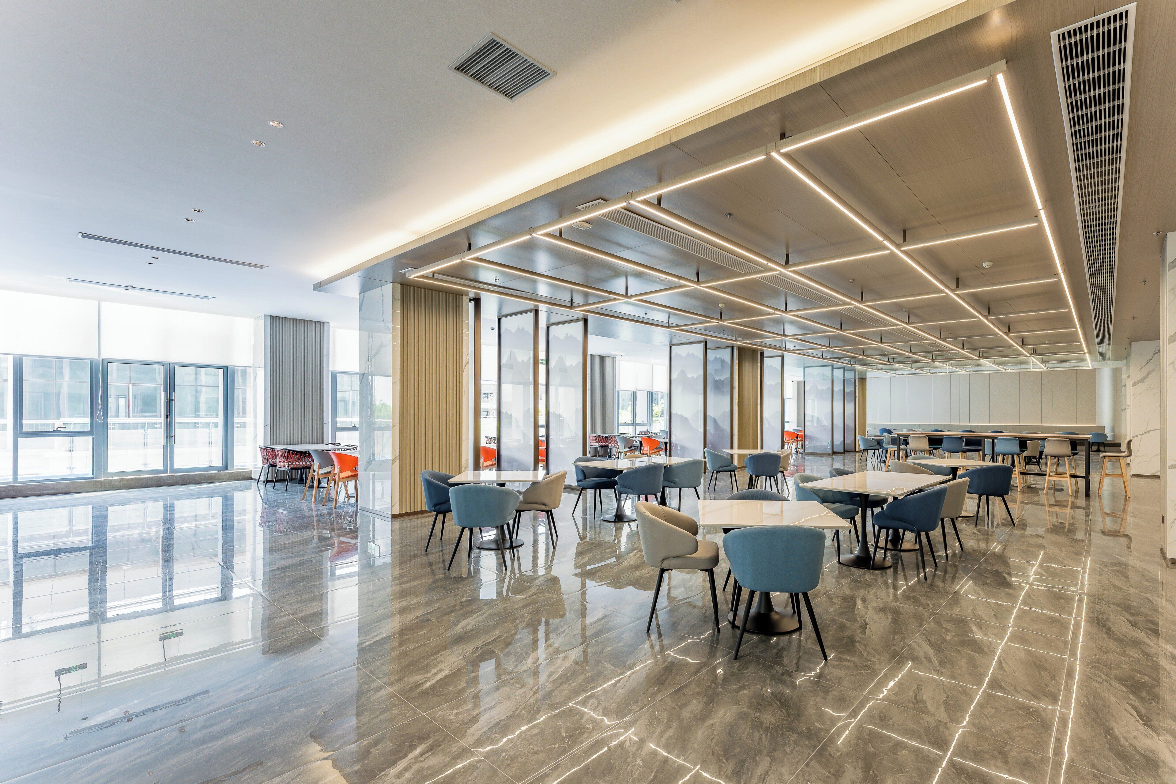 Un espacio interior amplio con mesas y sillas, ventanas grandes y un diseño moderno en el techo.