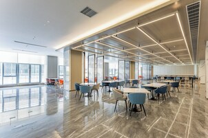 A spacious indoor area with tables and chairs, large windows, and a modern ceiling design.
