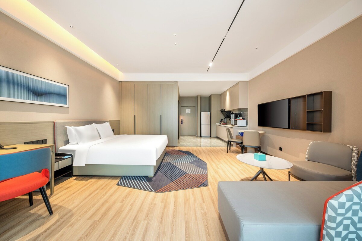 Una habitación de hotel moderna con una cama, un escritorio, una silla, un sofá y un televisor.