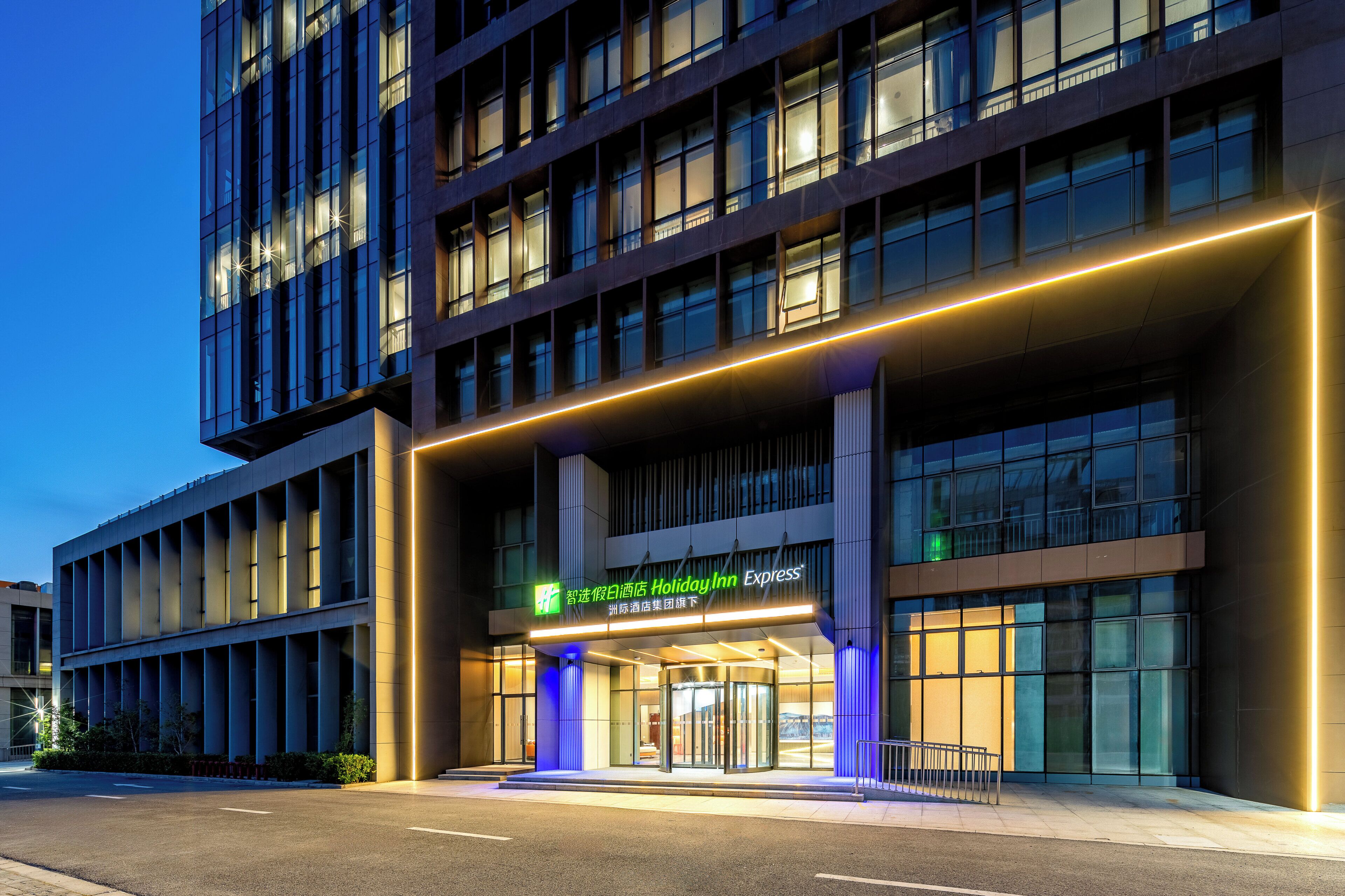 Un moderno edificio de hotel con una entrada destacada, amplias ventanas y señalización iluminada.