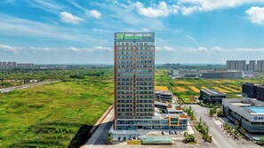 A high-rise building with a modern glass facade, surrounded by green fields and other buildings. - Holiday Inn Express Qidong Economic Zone by IHG (Nantong)