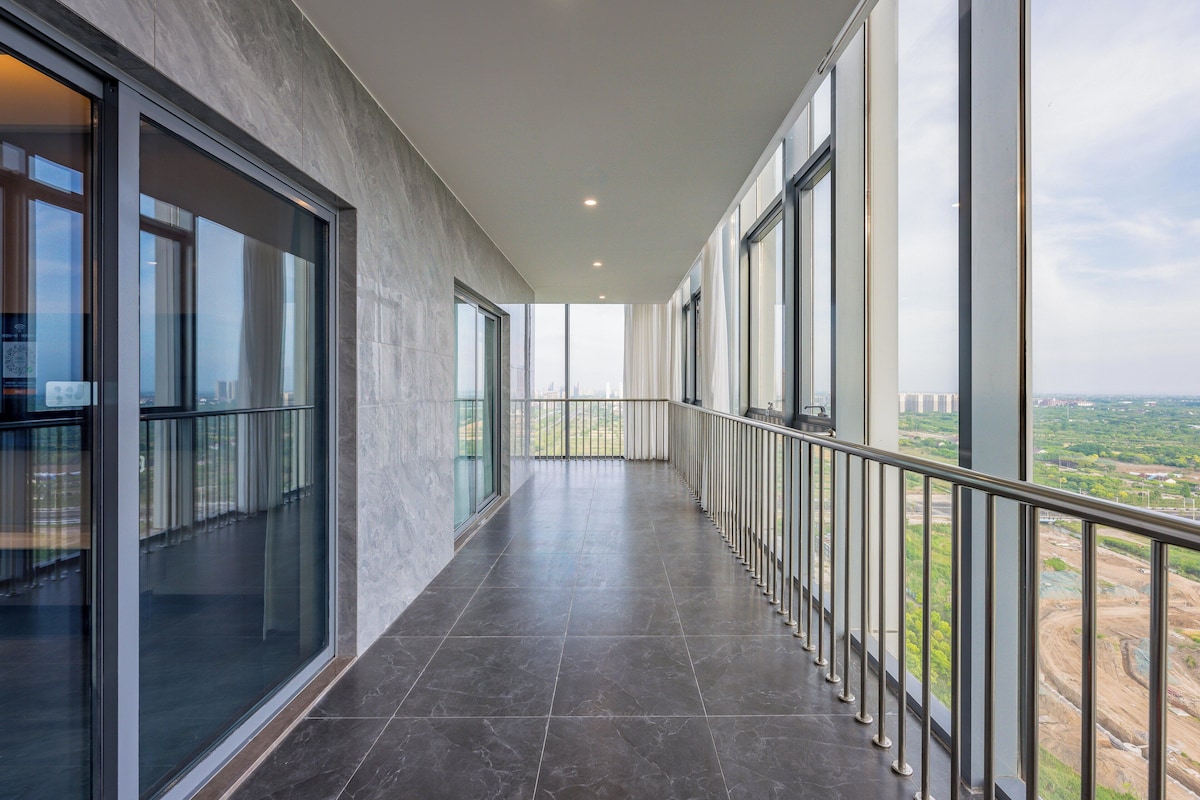 Un pasillo moderno con ventanas amplias, barandilla metálica y vista a una obra en construcción.