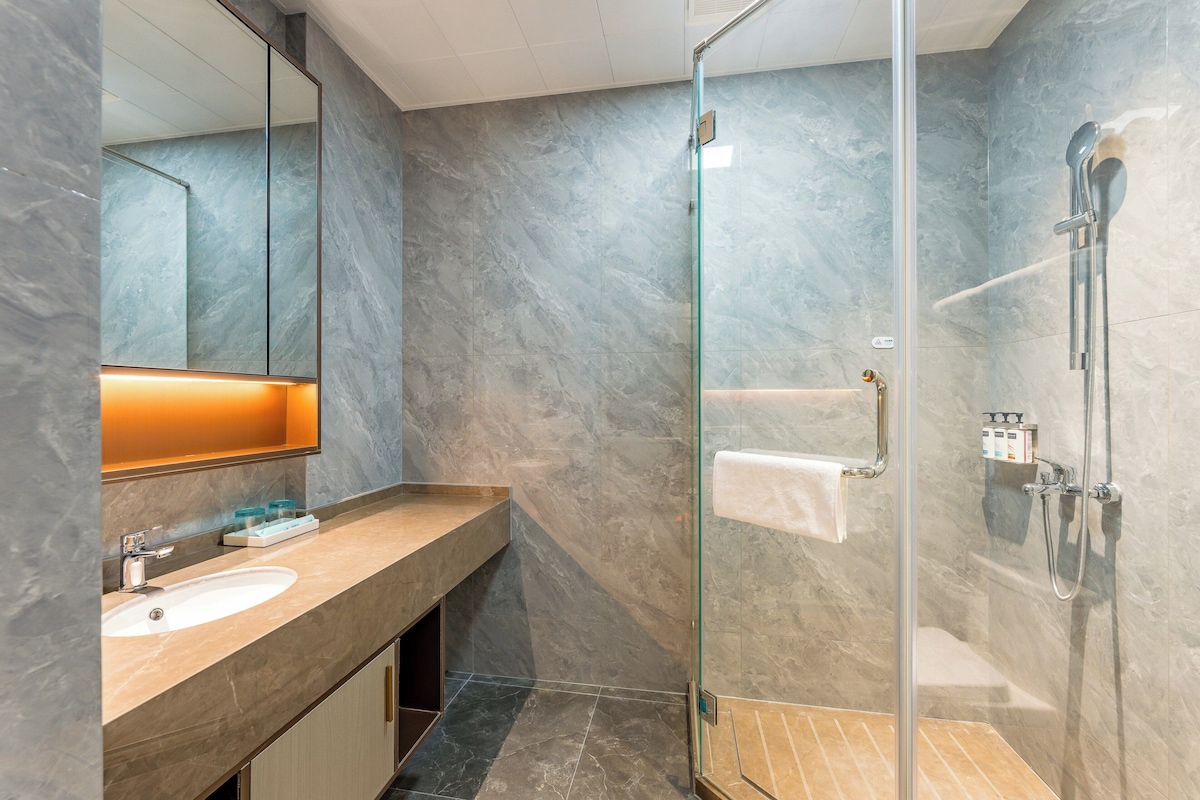 Un baño moderno con ducha envuelta en vidrio, pared de azulejos de mármol y lavamanos con espejo.