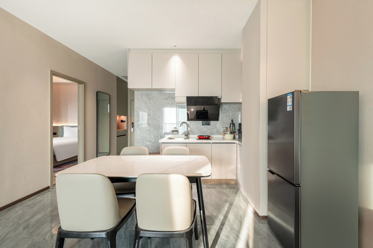 Una cocina moderna con una isla central, un refrigerador y un comedor con sillas.