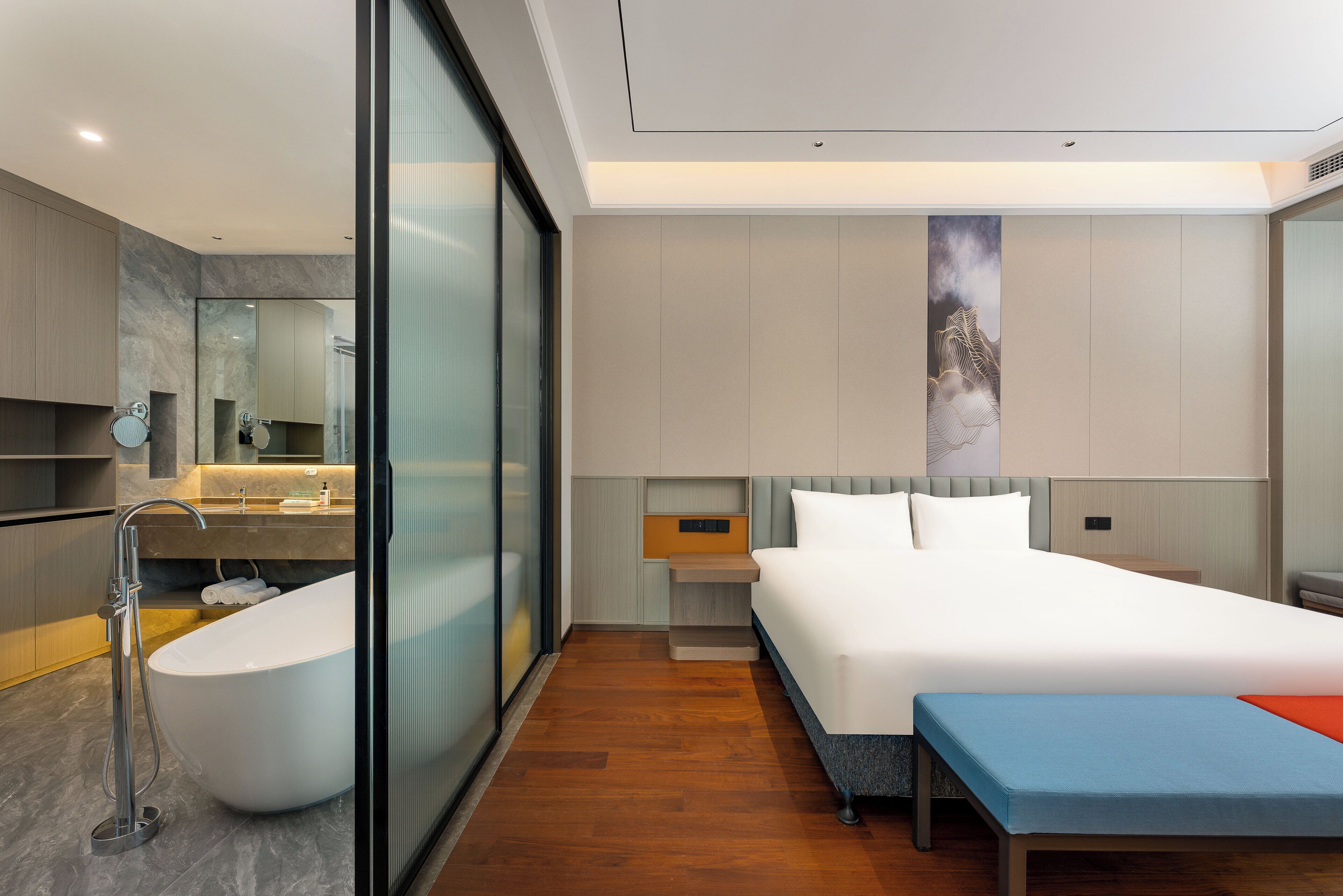 A modern hotel room with a large bed, a separate seating area, a bathroom with a bathtub, and a large mirror.